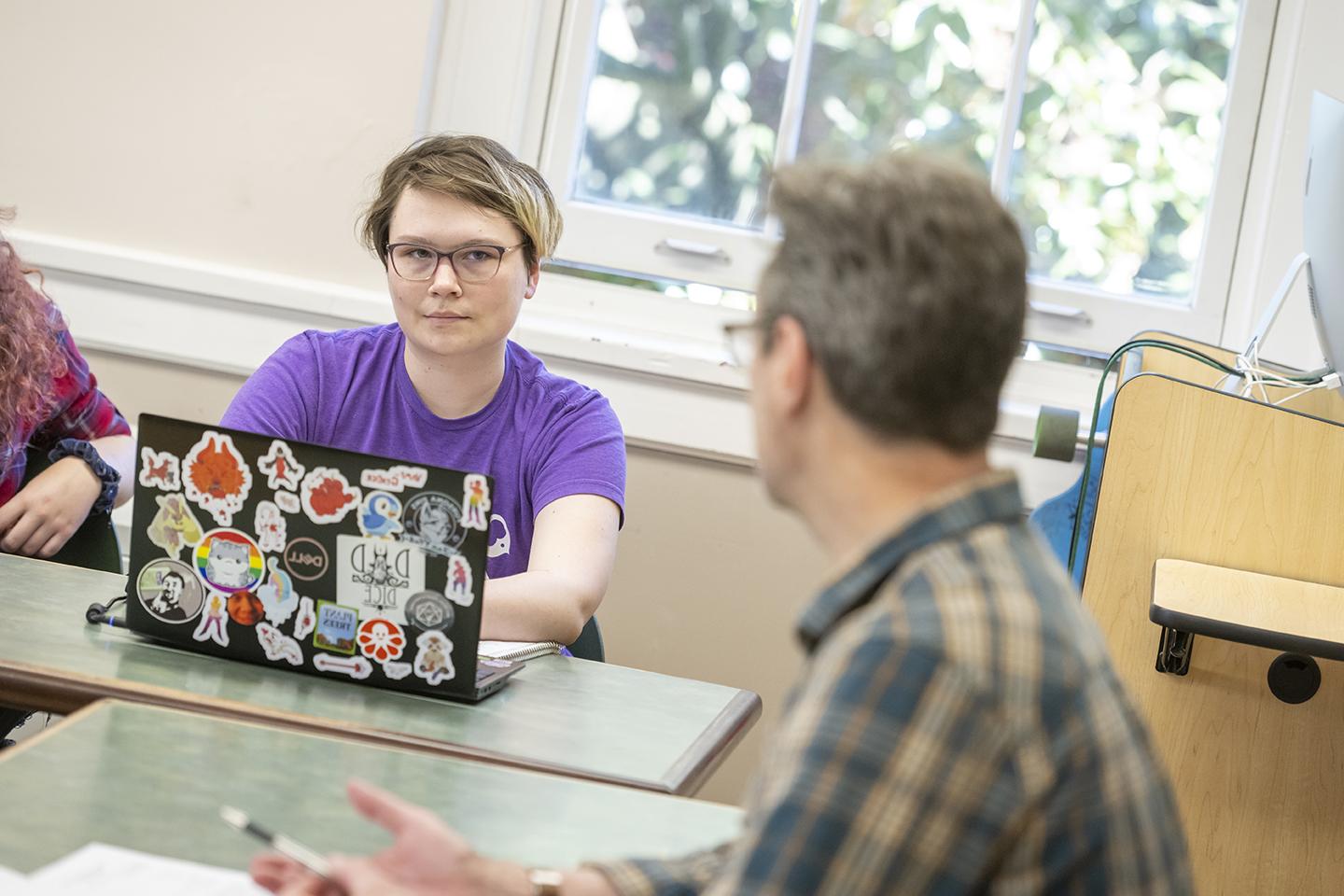 student writing on laptop listens to professor